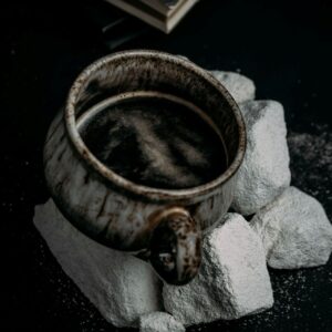 Rustic ceramic mug filled with dark broth, resting on pale stones; low, moody light.