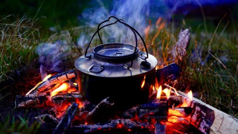 Black pot simmering over a small campfire with gentle smoke; outdoor dusk, minimalist scene.