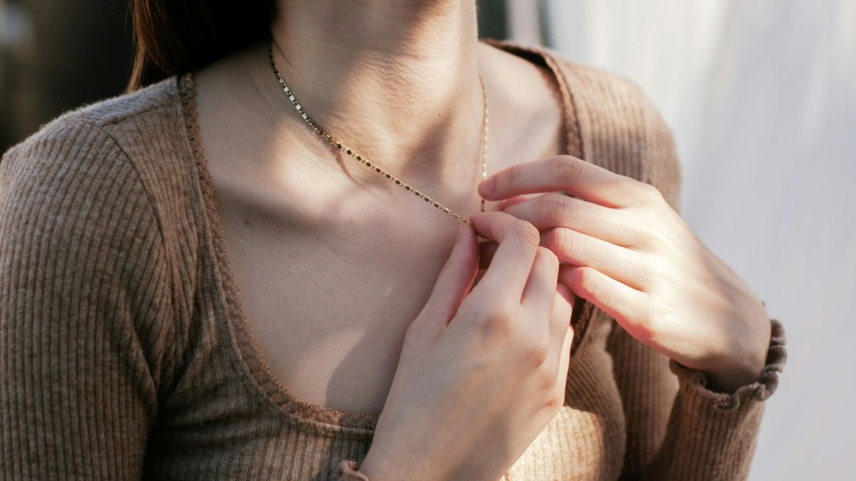 Silent Medicine — hands resting at the collarbone in a soft neutral sweater, gentle light.