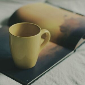 Warm mug resting on an open book in gentle light... a simple cue that chosen aloneness can feel nourishing.