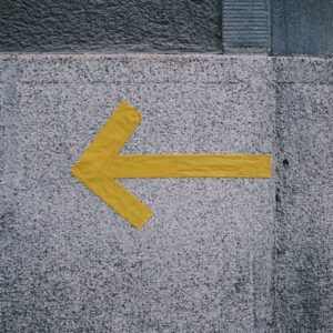 Yellow tape arrow pointing left on a concrete wall... a simple cue to choose one clear direction.