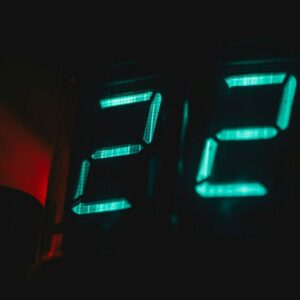 Close-up of bright blue digital clock numbers glowing in a dark room... an example of disruptive light at night in your sleep environment.