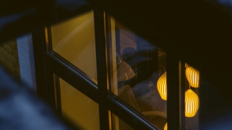 Warm pendant lamps glowing softly through a window at night, suggesting a calm, sleep-friendly environment.