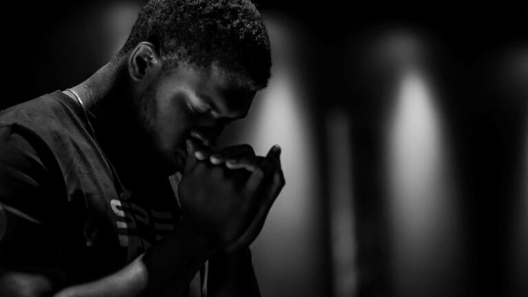 Black-and-white photo of a person with eyes closed and hands together, conveying quiet focus and reflection.