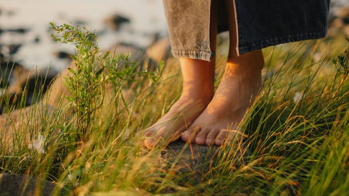 Bare feet on sunlit grass by rocks, suggesting simple grounding without gadgets.
