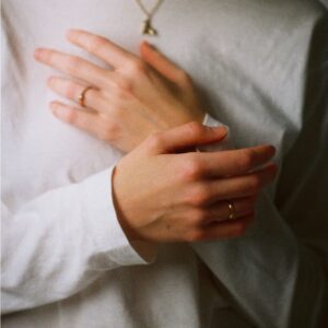 Close crop of hands resting over the heart on a white shirt, a gentle anchor for heart-focused breathing.