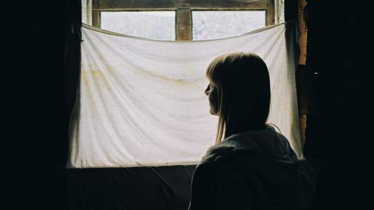Silhouette of a person by a curtained window in soft light... a disconnection from the world... a connection needed albeit in a noisy world.