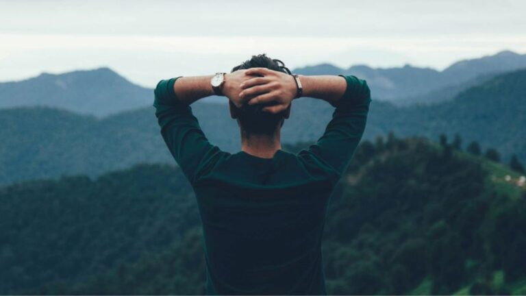 Person with hands behind head looking over misty mountains, pausing to choose a direction with a calmer mind.