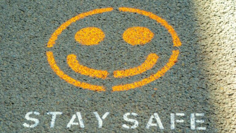Yellow smiley stencil and “STAY SAFE” on asphalt, suggesting simple home safety for electrical noise.