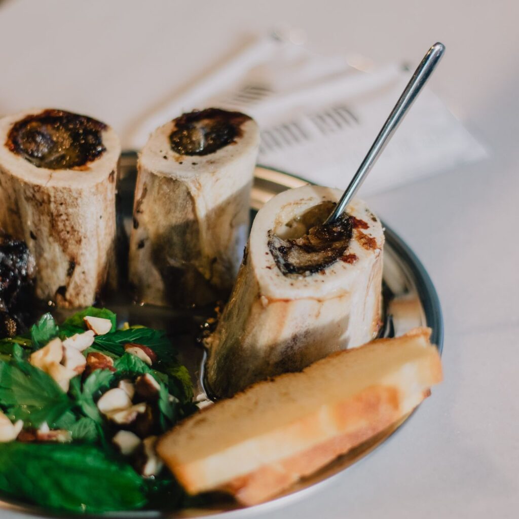 Three upright roasted marrow bones on a plate with a spoon