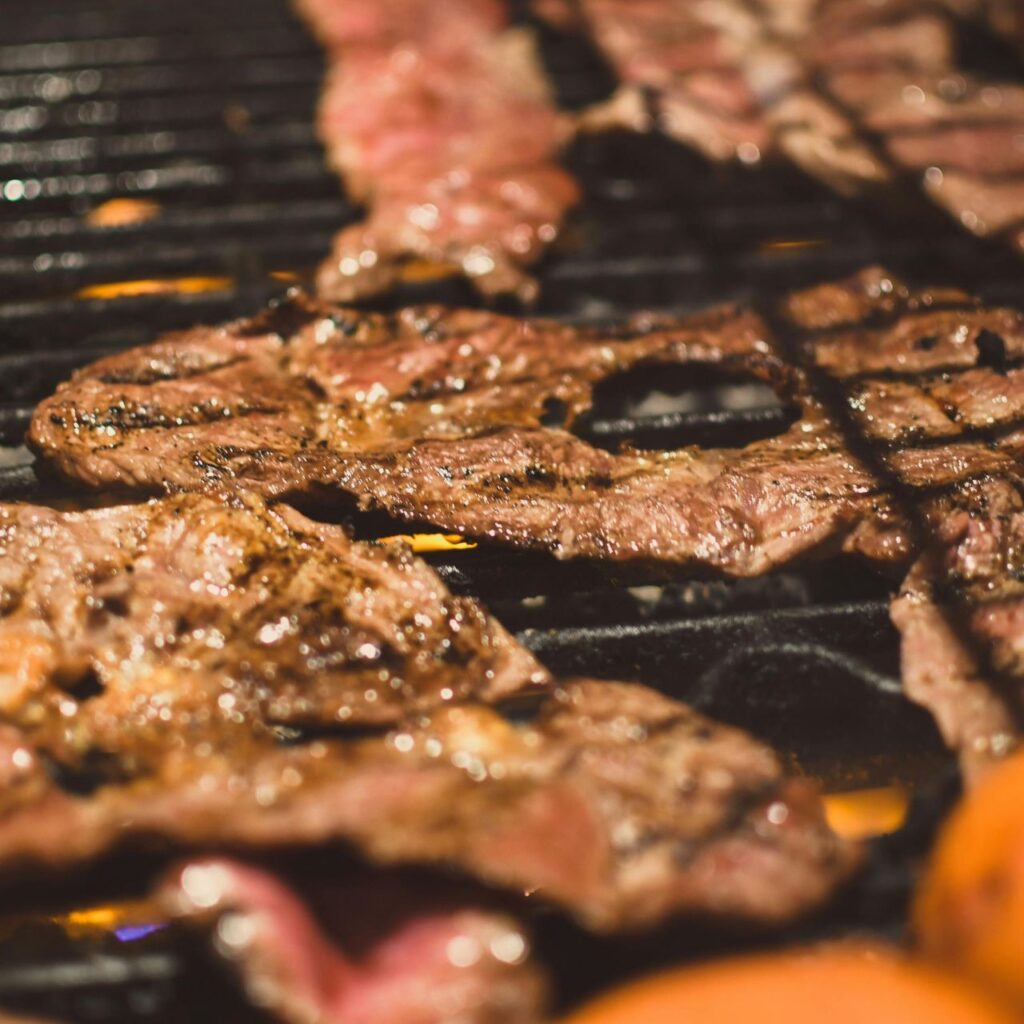 Thin beef patties cooking over high heat on grill grates with visible browning