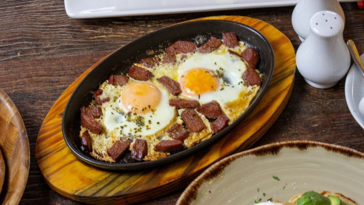 Oval skillet with browned beef and two softly set eggs on a wooden trivet