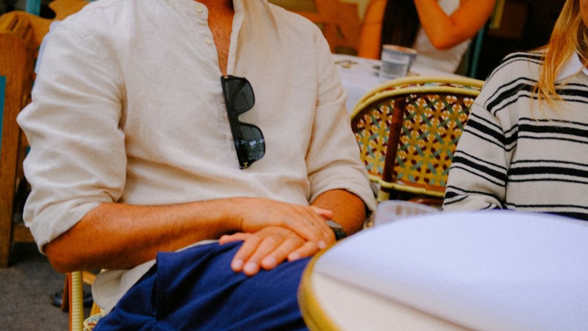 Person sitting at a café with relaxed shoulders and hands folded, illustrating a calm posture before a 2-minute reset.