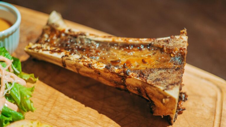Canoe-cut roasted bone marrow on a wooden board, glossy and jiggly