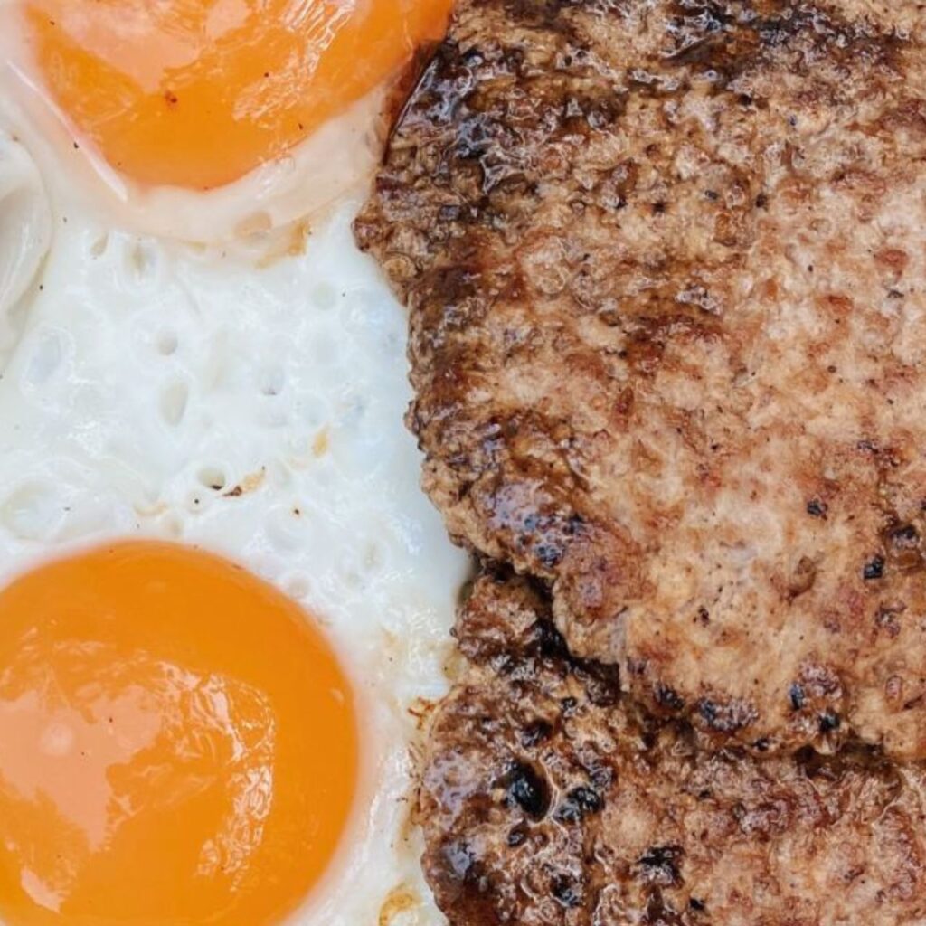 Close-up of tallow-poached eggs beside seared beef patties