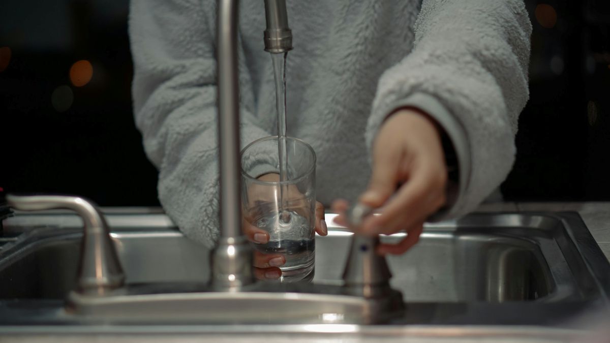 Person filling a clear glass with tap water at a kitchen sink.