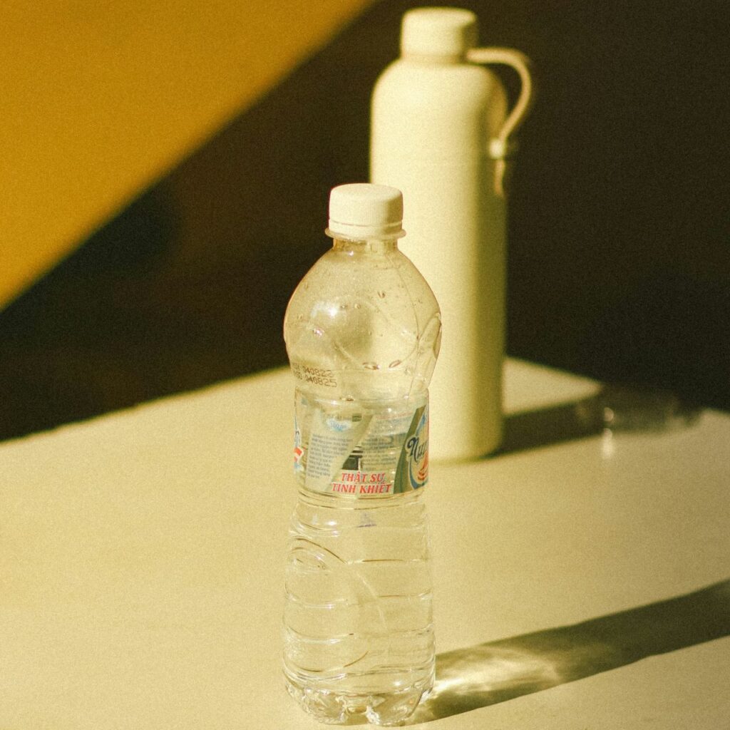 Reusable plastic bottle in front with stainless steel bottle behind on a light surface.