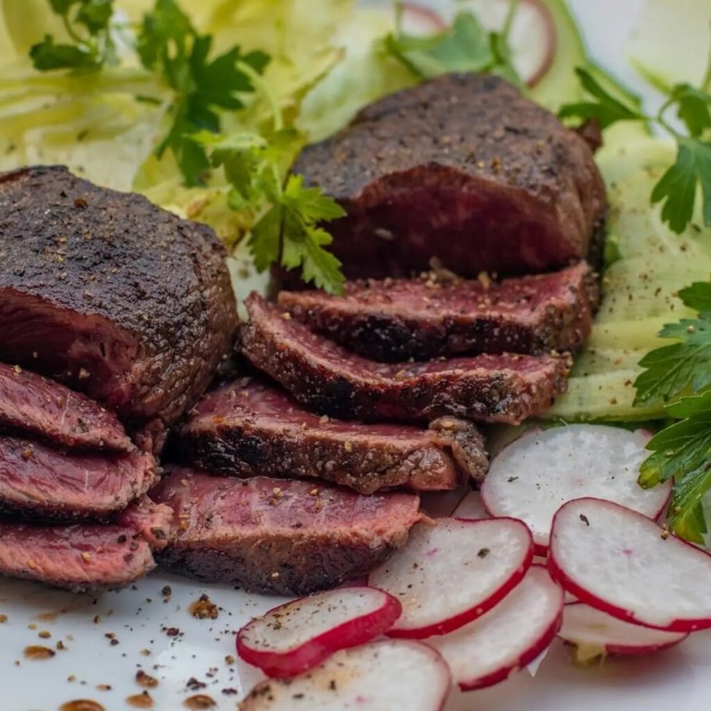 Sliced medium-rare beef tenderloin with simple sides on white plate.