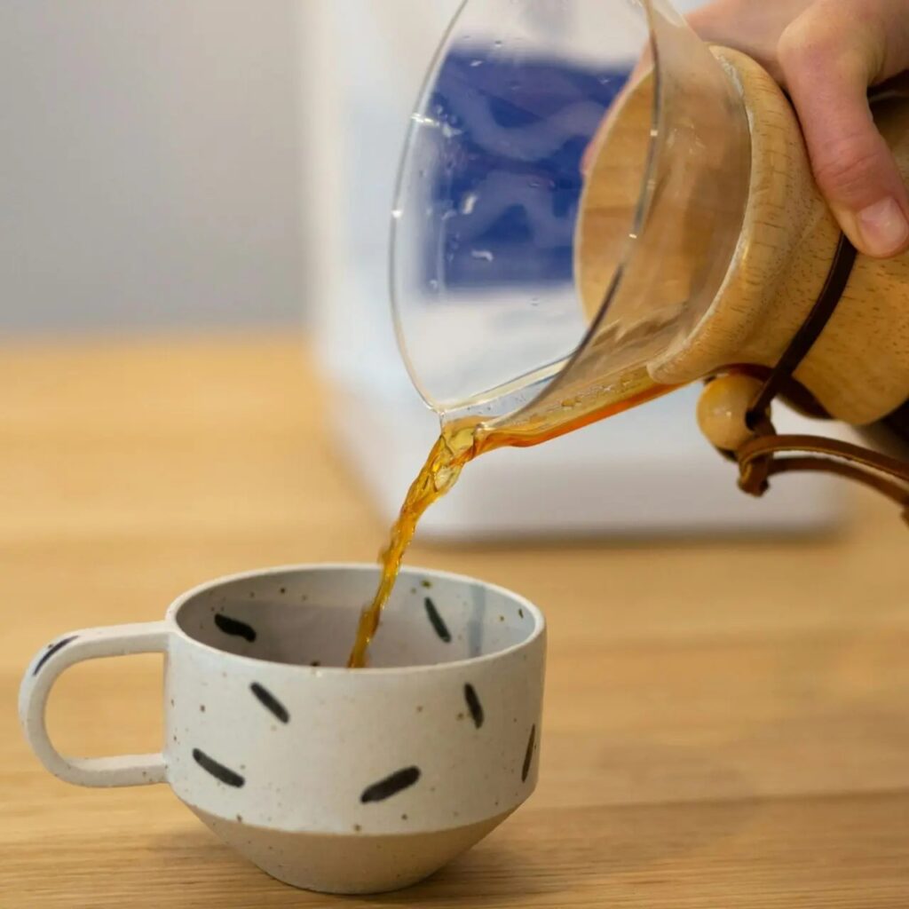 Amber broth poured from glass carafe into speckled mug.