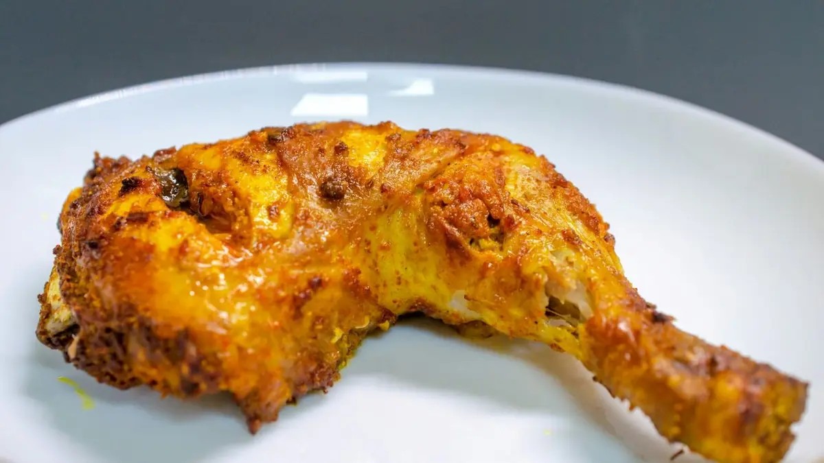 Crispy roasted chicken leg quarter on a plain white plate.