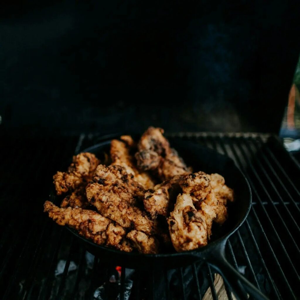 Golden crispy chicken pieces in a cast-iron skillet on grill.