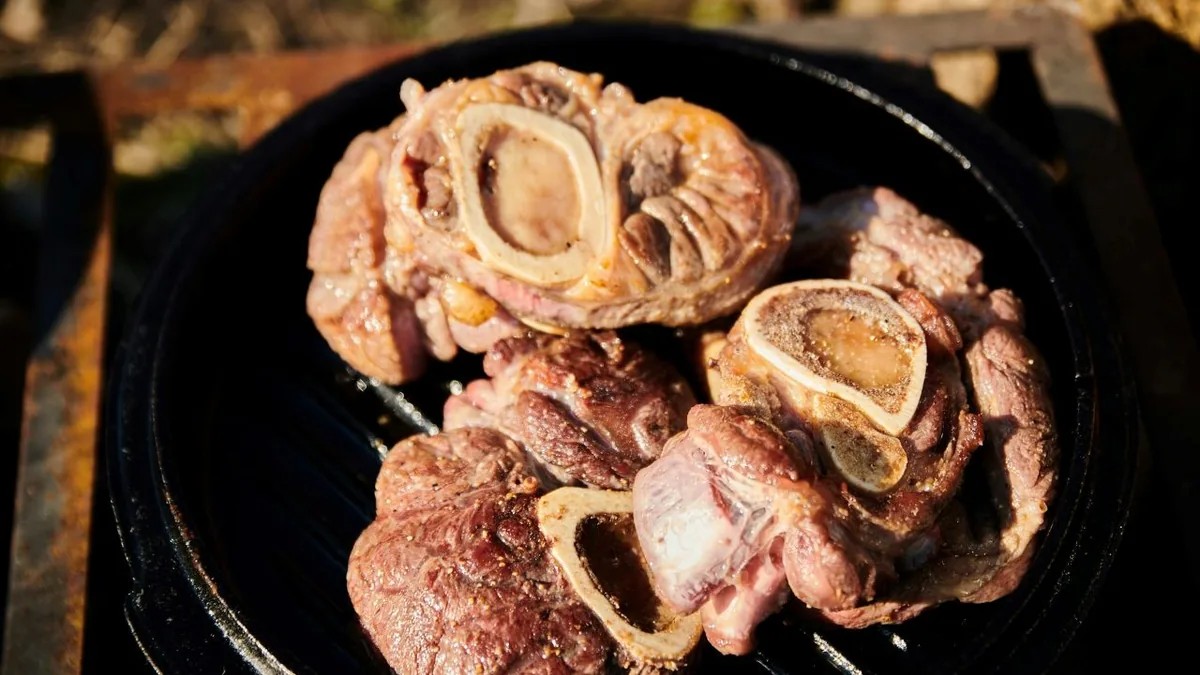 Browned oxtail pieces with exposed marrow on a hot grill.