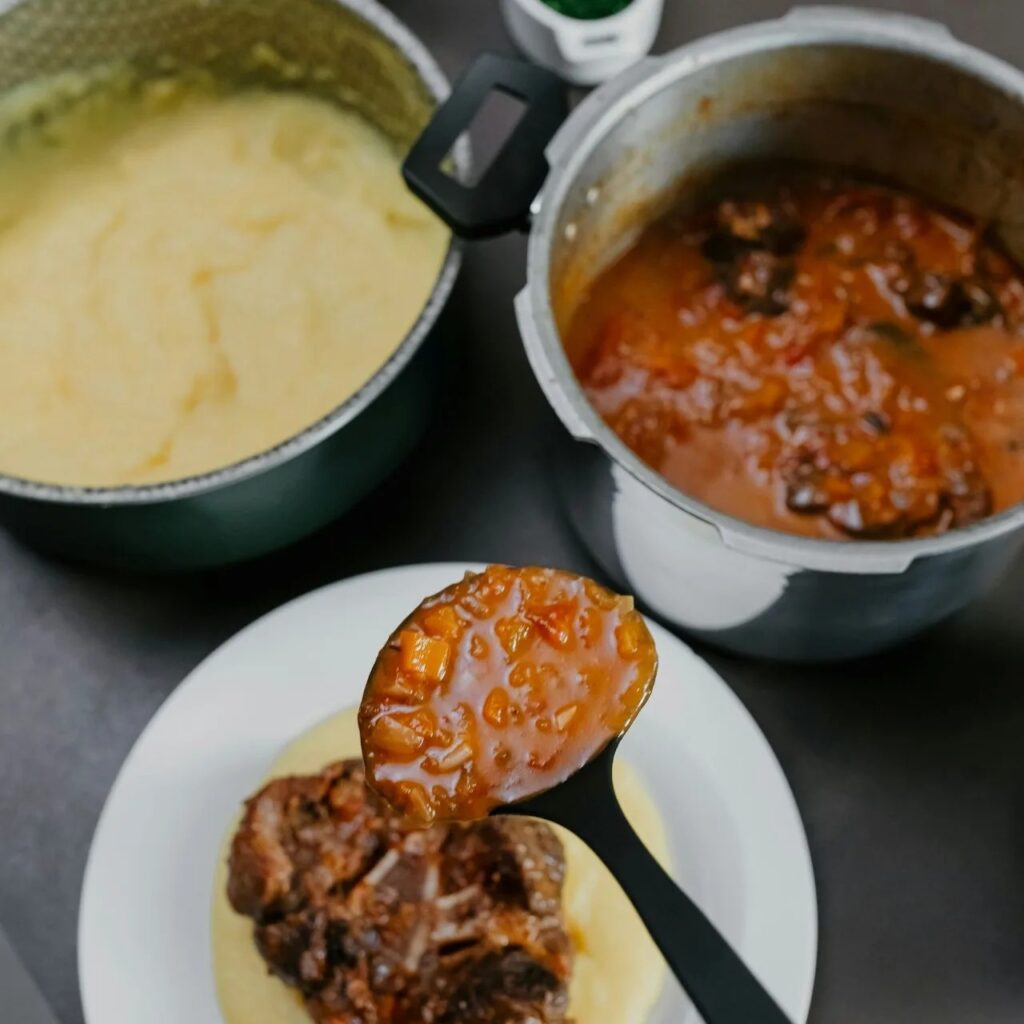 Ladle of tomato-carrot sauce over tender oxtail on plate.