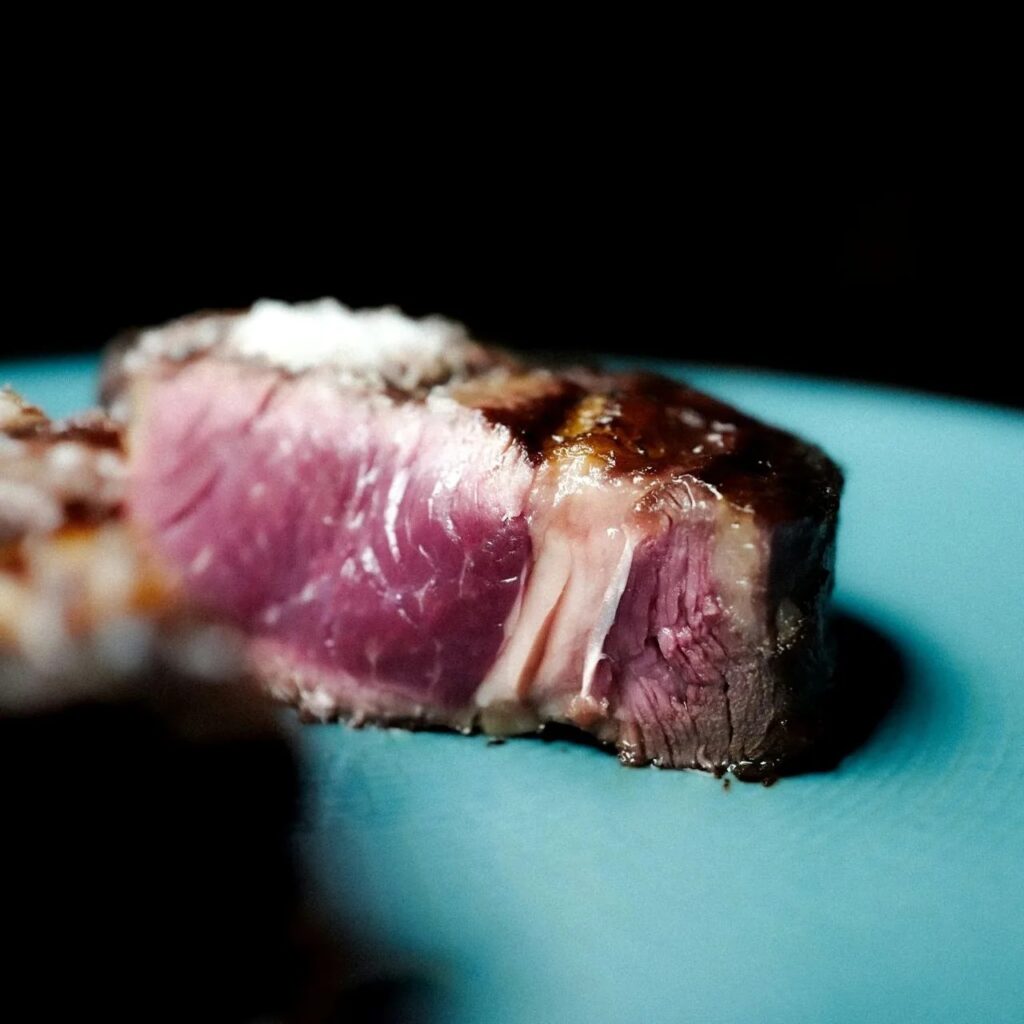 Close-up ribeye slice with pink center on a blue plate.