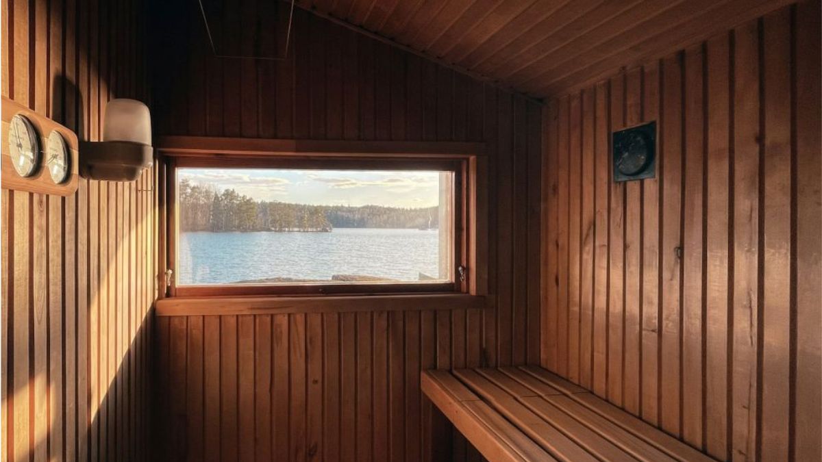 Warm wooden sauna interior with sunlight and a small window to a lake.