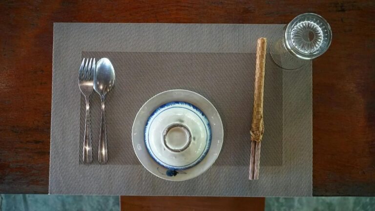 Minimal table setting with spoon and fork resting beside a small plate and glass on a placemat, pausing before eating.