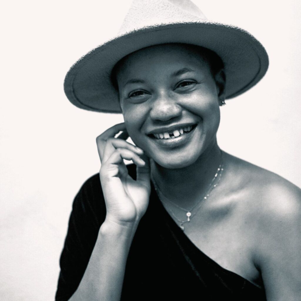 Smiling person wearing a hat with relaxed shoulders, calm expression on a light background.