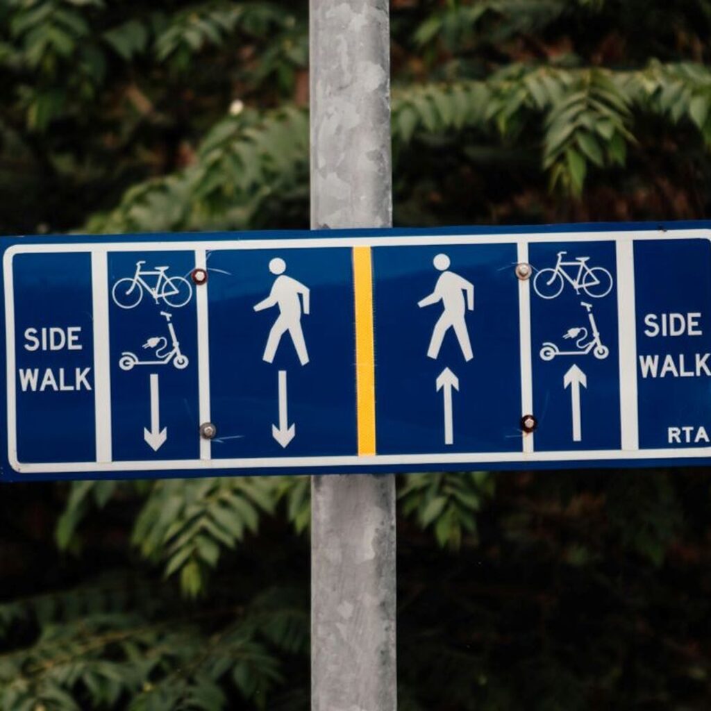 Blue route sign showing sidewalk and bike/scooter lanes with arrows indicating directions.