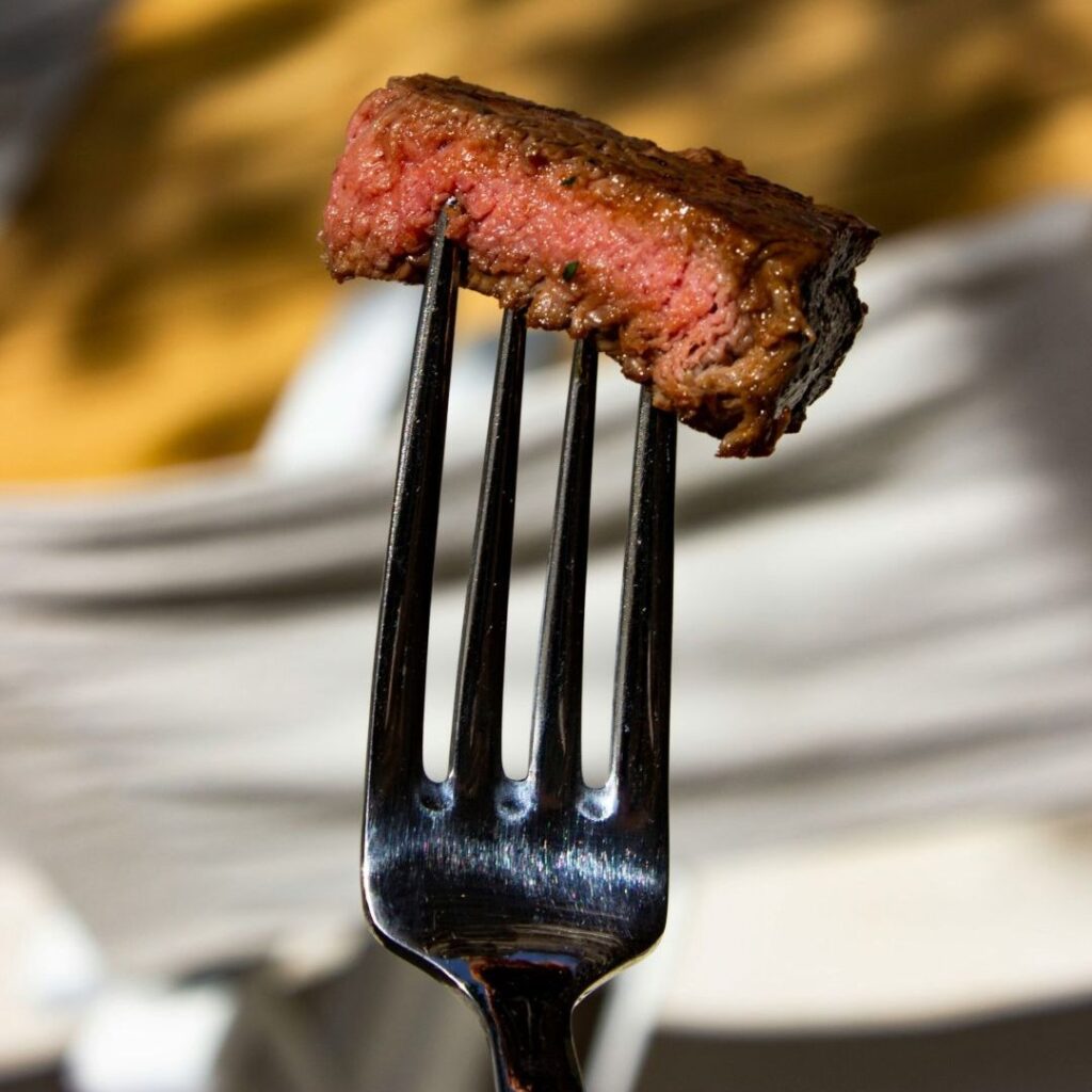 Close-up of a medium-cooked piece of steak on a fork with a softly blurred background.