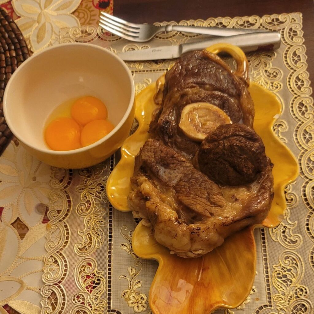 Cooked beef chuck-o-bone roast on a yellow plate with three egg yolks in a small bowl.