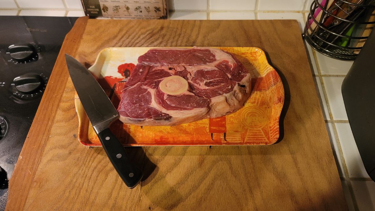 Raw grass-fed beef chuck-o-bone roast with a knife on a tray beside the stovetop.