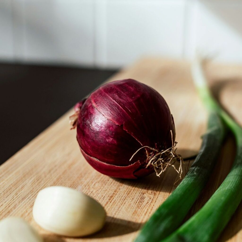 red onion, green onion stalks, and garlic cloves on a wooden cutting board in soft light