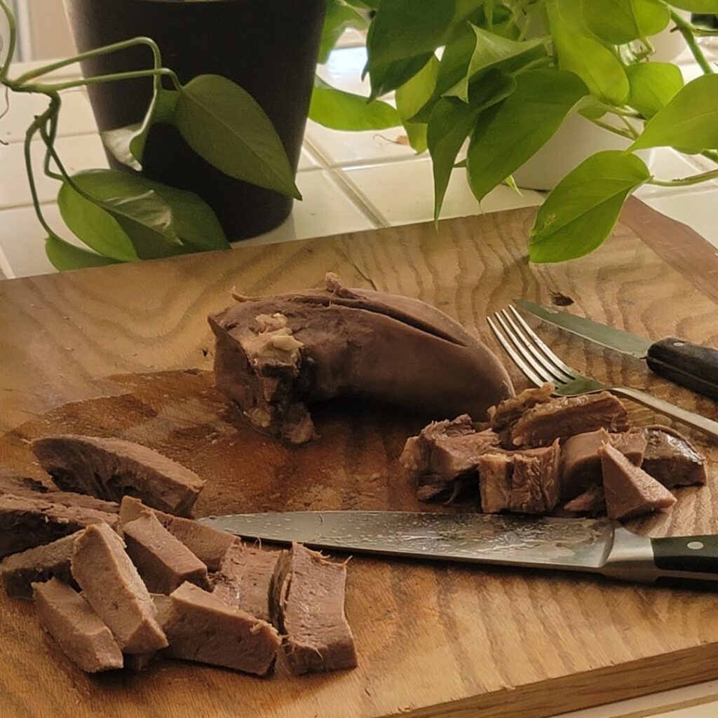 Cooked beef tongue sliced into cubes and strips on a wooden cutting board.