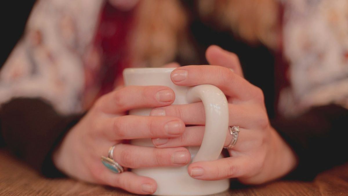 Hands holding a white mug on a wooden table