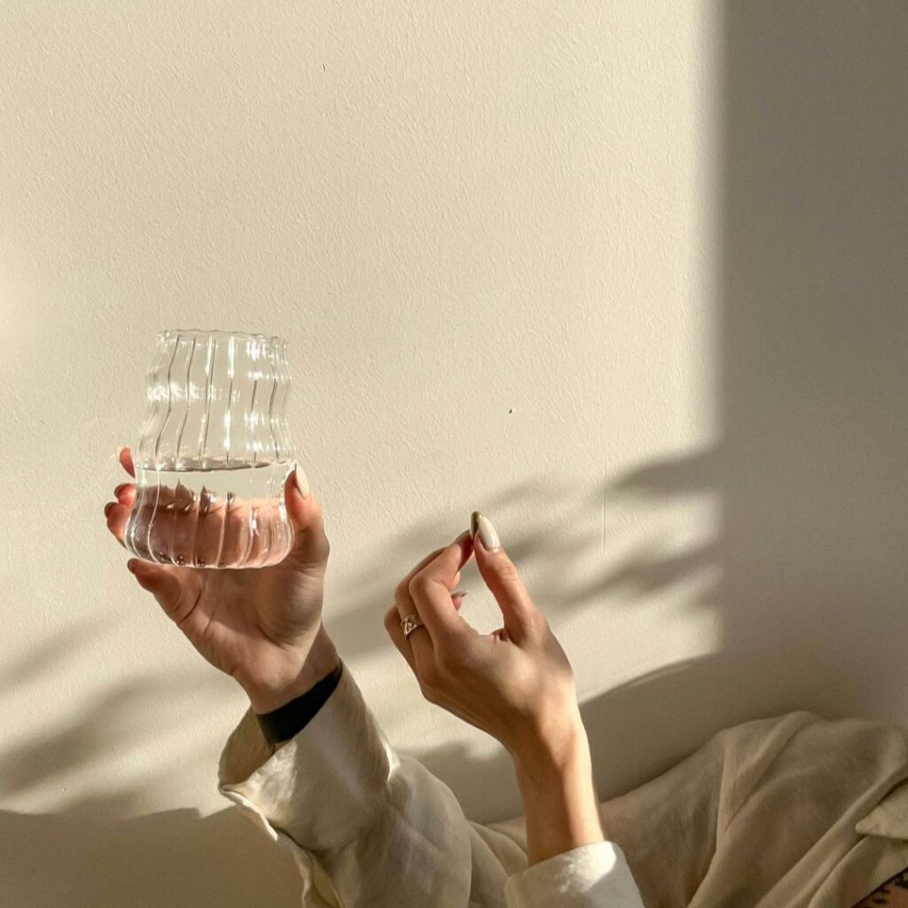 Hands holding a glass jar of water and a mineral tablet in soft sunlight