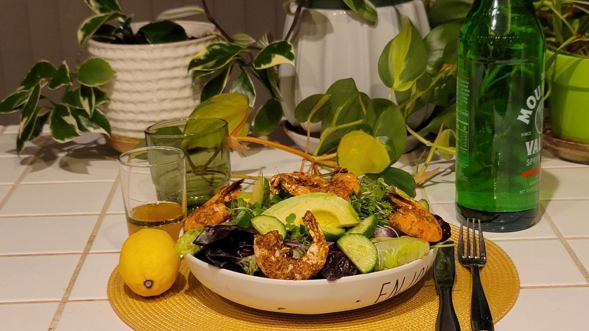 Spiced shrimp and mixed greens salad with avocado, cucumber, and lemon on a kitchen counter