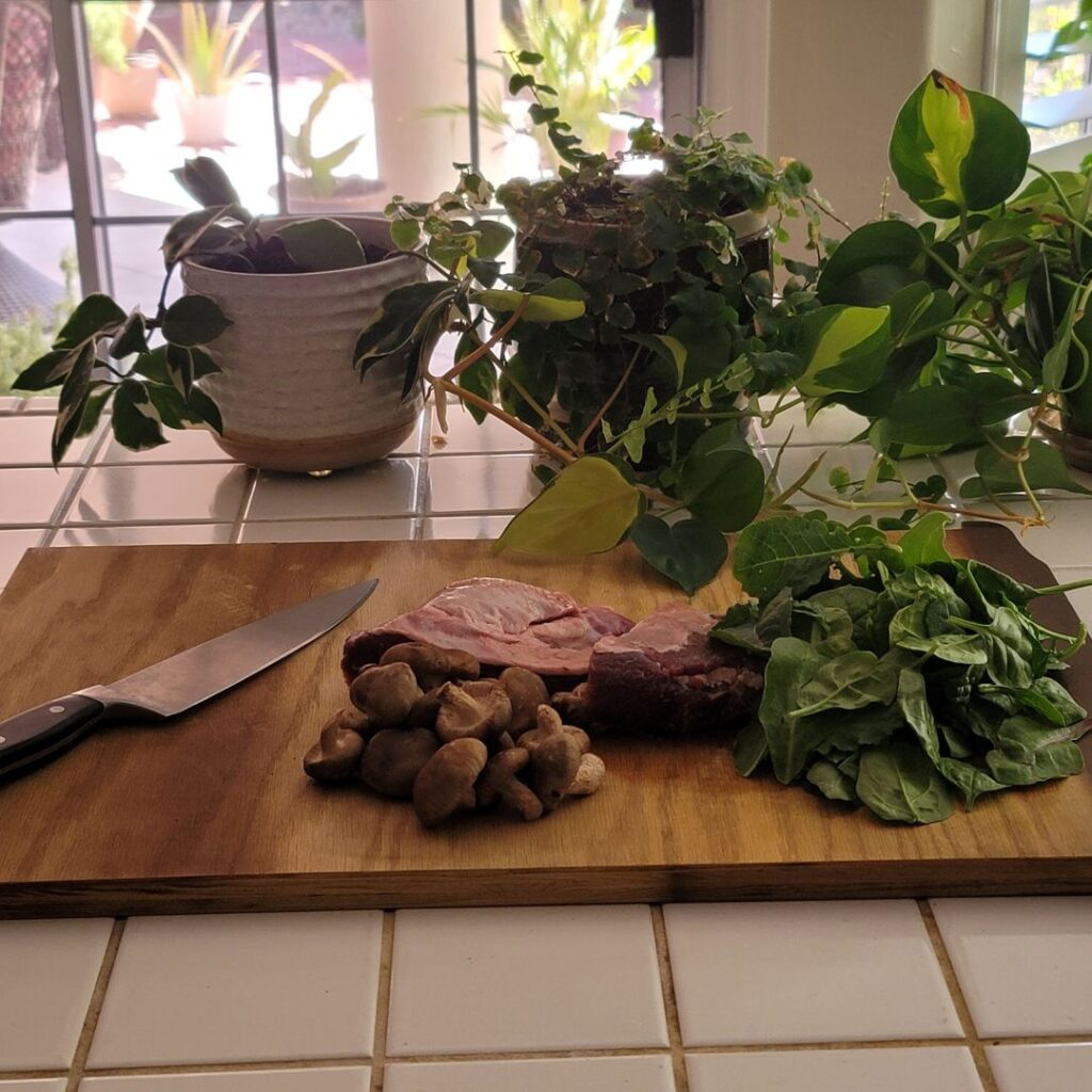 Raw cheek meat with mushrooms, greens, ginger, turmeric, and citrus on a wooden board