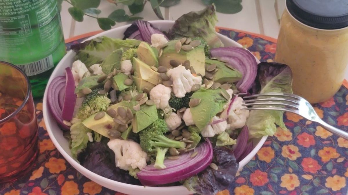 A vibrant raw ketovore bowl with broccoli, cauliflower, avocado, pumpkin seeds, onions, and lemon-ginger dressing.