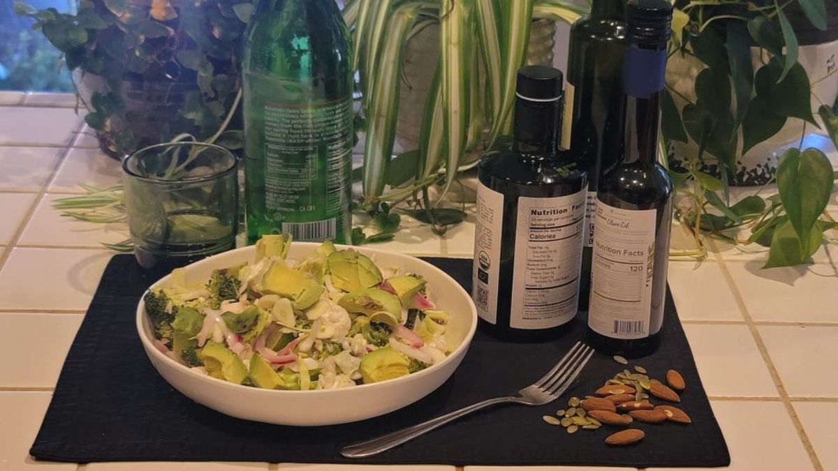 Raw ketovore vegetable bowl with avocado, olive oil, almonds, pumpkin seeds, and fresh vegetables on a calm kitchen counter surrounded by plants