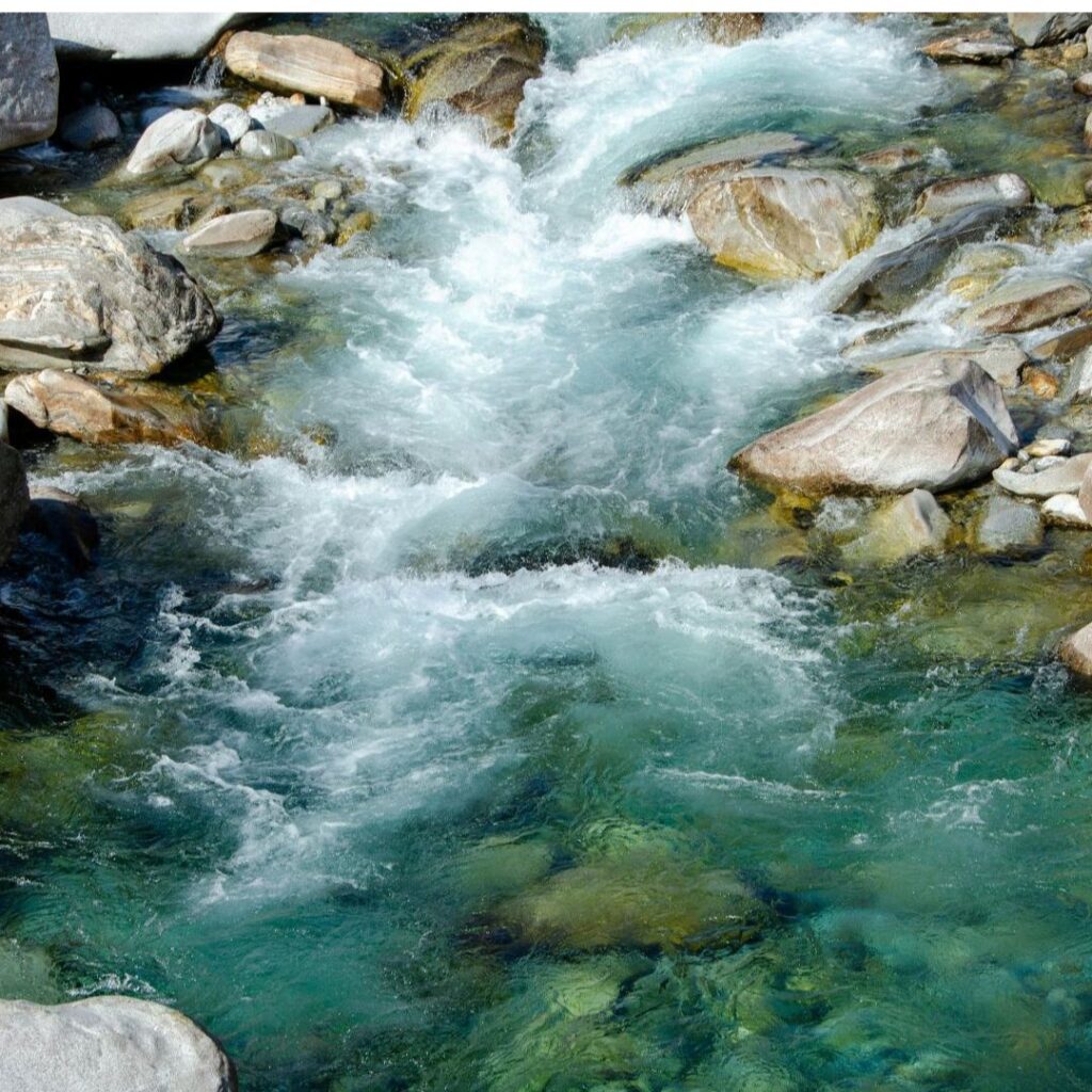 Clear flowing water moving around rocks in a mountain stream, symbolizing adaptation, transformation, and forward movement.